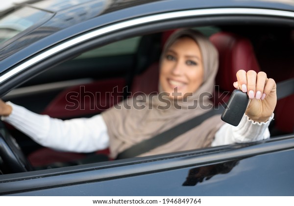 Smiling Arabic Woman In Hijab Showing Car Keys\
Sitting In Her New Vehicle On Driver\'s Seat. Middle East Female\
Choosing Auto Transport In Dealership Showroom Store. Selective\
Focus, Blurred\
Background