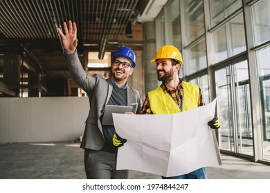 Smiling architect holding tablet and showing to construction worker something he imagined. Construction worker holding blueprints. Construction site interior. - Powered by Shutterstock