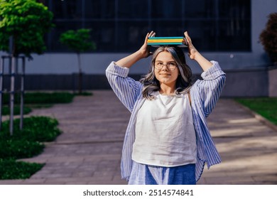 Smiling Armenian girl with glasses balances a stack of books on head in school backyard urban background. Ready for school. Back to school concept. - Powered by Shutterstock