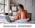 Smiling asian accountant woman working with documents using calculator and laptop computer at office desk