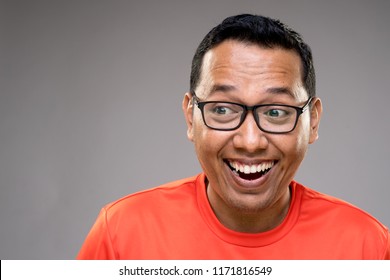 Smiling Asian Adult Male Wearing Orange T-shirt With A Quirky And Funny Reaction On A Grey Toned Background