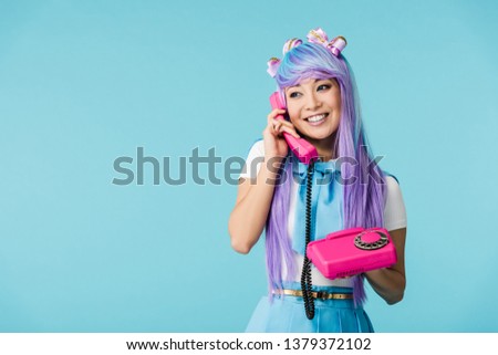 Smiling asian anime girl talking on telephone isolated on blue