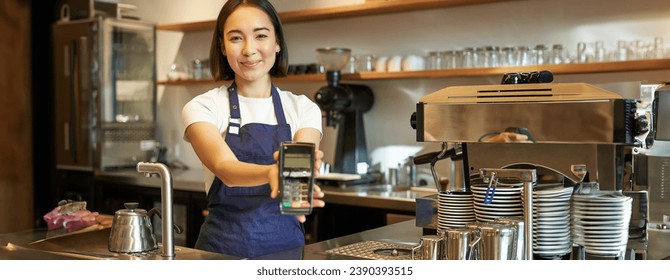 Smiling asian barista, coffee shop staff gives you credit card machine, processing payment with POS terminal, working in cafe. - Powered by Shutterstock