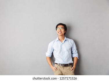 Smiling Asian Business Man Standing Isolated Over Gray Background, Looking Away