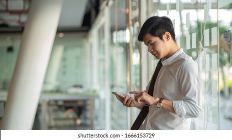 Smiling Asian Business Man Standing, Using Mobile Phone.