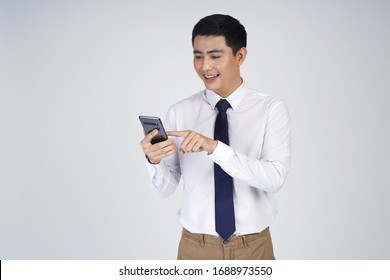 Smiling Asian Business Man Standing Isolated Over Gray Background, Using Mobile Phone