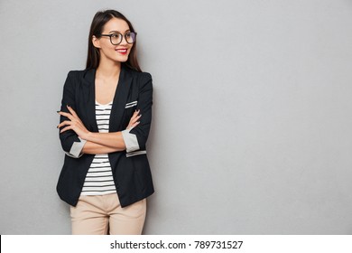 Smiling Asian Business Woman In Eyeglasses With Crossed Arms Looking Away Over Gray Background