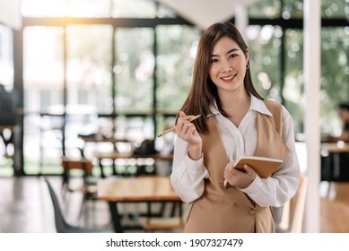 Smiling Asian Business Woman Holding A Notebook And Pencil At The Office. Looking At Camera.