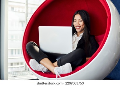 Smiling Asian Business Woman Using Laptop Computer Sitting Inside Ball Chair At Modern Office 