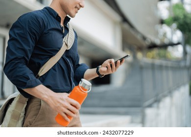 Smiling asian businessman hold reusable eco-friendly ecological cup and using mobile while on the way home at park - Powered by Shutterstock