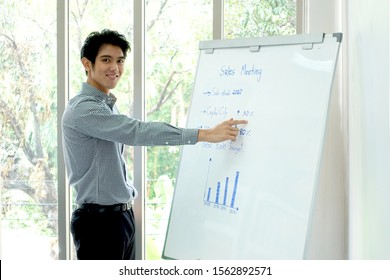 Smiling Asian businessman looking straigth confidently while preseting the sales chart. For corporate, business, finance, management, communication and technology concept. - Shutterstock ID 1562892571