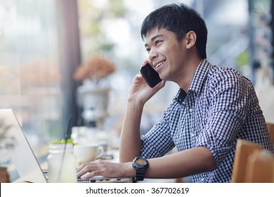 Smiling asian businessman making a call during relax with notebook in coffee shop - Powered by Shutterstock