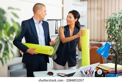 Smiling Asian Businesswoman Standing With Male Colleague In Office Holding Yoga Matts. Corporate Fitness For Employee Concept