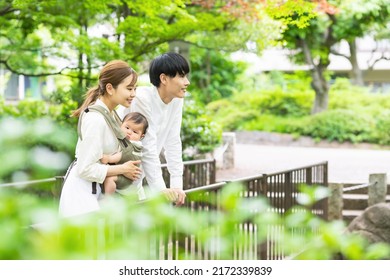 Smiling Asian Couple And Baby Relaxing In Green Park. Child Rearing. Newborn.