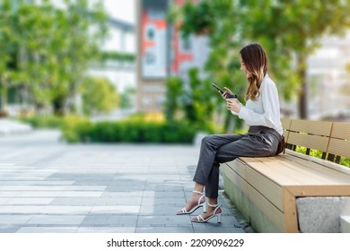 Smiling Asian Curly Business Woman Wearing Trendy Walks Down The Central City Street And Uses Her Phone. Pretty Summer Woman In White Shirt Walks Down The Street Looking At Her Mobile Phone