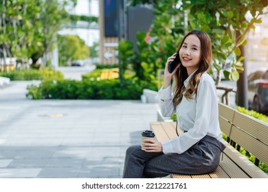 Smiling Asian Curly Business Woman Wearing Trendy Walks Down The Central City Street And Uses Her Phone. Pretty Summer Woman In White Shirt Walks Down The Street Looking At Her Mobile Phone