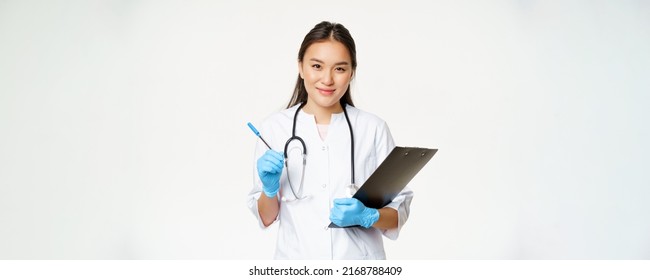 Smiling Asian Doctor, Female Nurse Holding Clipboard And Pen, Wearing Uniform With Gloves, Writing Patient Information, Standing Over White Background