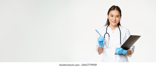 Smiling asian doctor, female nurse holding clipboard and pen, wearing uniform with gloves, writing patient information, standing over white background. - Powered by Shutterstock