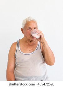 Smiling Asian Fat Old Man In Undershirt Drinking Milk With His Left Hand On Blank Background.