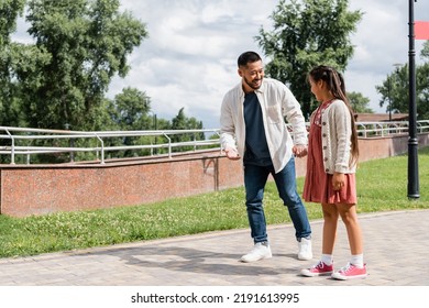 Smiling Asian Father Holding Hand Of Daughter And Talking In Park