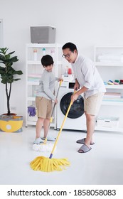 Smiling Asian Father And Little Boy Child Is Enjoying For House Cleaning Together In Laundry Room. They Is Mopping The Floor. Family Time On Holiday Concept