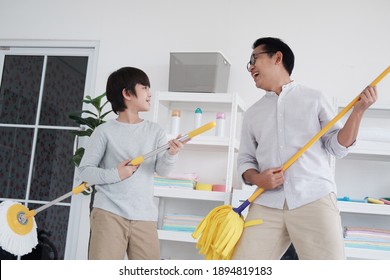 Lächelnder asiatischer Vater und kleines Kind genießt das Haus Reinigung zusammen im Waschraum. Sie singen im Urlaub mit dem Mopp für Gitarre spielen.