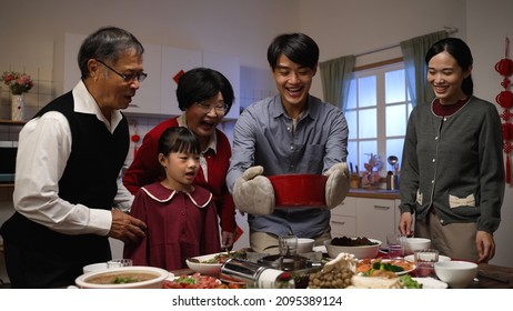 Smiling Asian Father Serving Hot Soup On The Dining Table And Posing With Folded Arms, Feeling Proud Of His Cooking. Preparing Food For Family On Chinese New Year's Eve