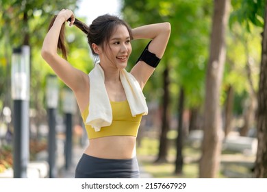 smiling asian female active sport lifestyle warmup stretching before running exercise while arranging her hair in the park morning workout healthy lifestyle well being life