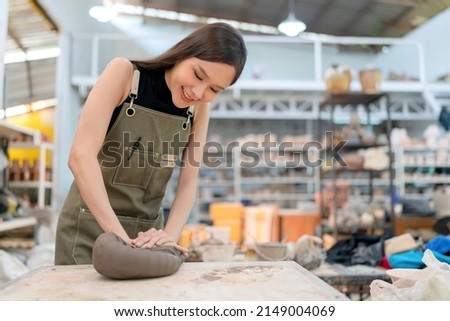 smiling asian female artist potters in aprons sculping clay ceramic product on working table in workshop. asia young female standing near hand makeing clay the art of pot making in factory