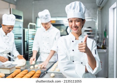 Panaderas asiáticas sonrientes mirando la cámara... Cocina casera con un traje y sombrero de chef. Equipo de cocineros profesionales en uniforme que preparan las comidas para un restaurante en   cocina.