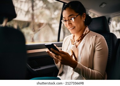 Smiling Asian Female CEO Sitting On The Backseat And Using Smart Phone While Going On A Business Trip By Car.