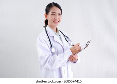 Smiling Asian Female Doctor Puts A Stethoscope On Her Shoulder.
Wearing A White Lab Coat Standing Holding A Note Board On Gray Background