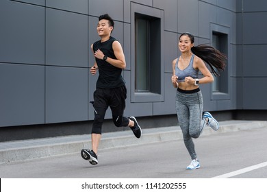 Smiling Asian Female And Male Athletes Running At Urban Street 