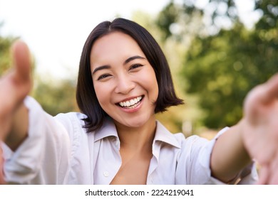 Smiling asian girl takes selfie, video chats, holds smartphone and speaks at camera, posing in park. - Powered by Shutterstock