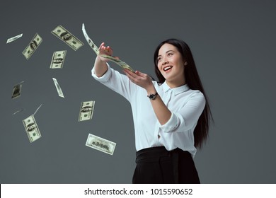 smiling asian girl throwing dollar banknotes isolated on grey