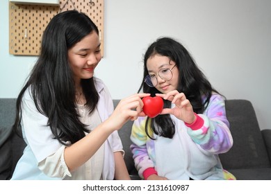Smiling Asian girl wearing medical uniform pretending to be doctor playing with her younger sister at home.