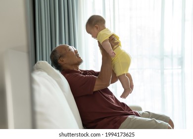 Smiling Asian Grandfather Playing Holding With His Cute Baby Boy. Senior Man Having Fun Lifting His Grandchild At Home. Family, Happiness And Love Concept