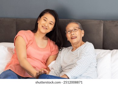 Smiling Asian grandmother and granddaughter sitting together on bed, enjoying time. Family, bonding, intergenerational, happiness, togetherness, love - Powered by Shutterstock