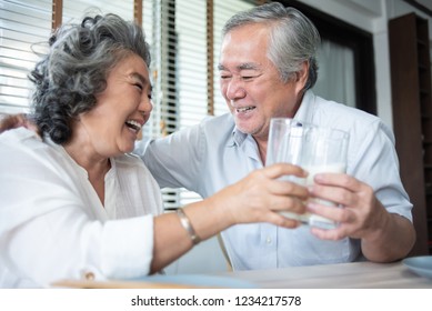 Smiling Asian Grandmother And Grandfather Drinking Milk Together At The Table. Happy Older Man And Woman Having Fun And Laughing During Breakfast In The Morning.