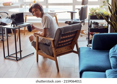 Smiling Asian Guy Holding Cup While Working With Laptop At Home