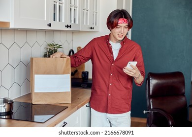 Smiling Asian Guy Holding Smartphone While Receiving Food Delivery