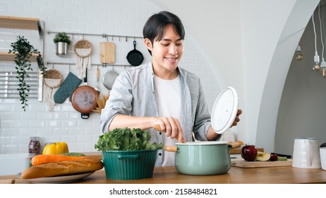 Smiling Asian Handsome Man Cooking In Kitchen At Home.Young Asian Male Chef Cooking Romantic Dinner At Home Taste Soup.