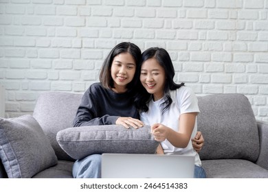 Smiling Asian lesbian couple using tablet for entertainment on sofa at home. LGBT lesbian moments. - Powered by Shutterstock
