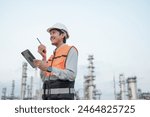 Smiling Asian male engineer wearing safety uniform standing in front of oil refinery with tablet device Radio communication to monitor oil refinery operations Petrochemical Gas Industry Engineer