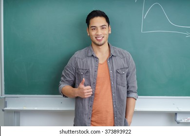 Smiling Asian Male Student Standing In Front Of The Chalkboard In The Classroom Giving A Thumbs Up Of Success And Approval With A Happy Smile