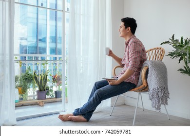 Smiling Asian Man Drinking Coffee Relaxing On The Couch At Home