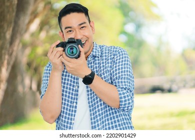 Smiling Asian man holding camera in the park,photographer with smiling face.