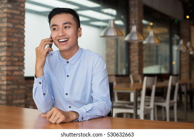 Smiling Asian Man Talking On Phone At Cafe Table