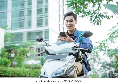 Smiling asian man using a cellphone while riding a motorcycle