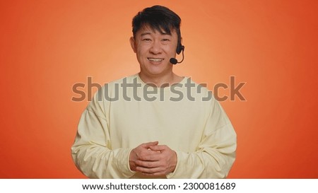 Smiling asian man wearing headset, freelance worker, call center or support service operator helpline, having talk with client or colleague, communication support. Handsome guy on orange background